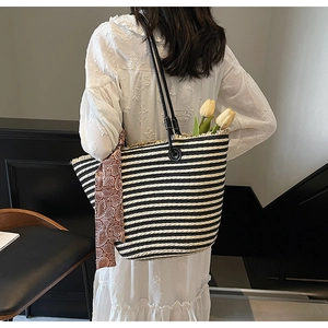 Detail of hand-woven black and white striped straw tote bag with elegant silk scarf