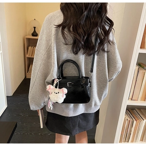 Detail view of black glossy crossbody bag with silver buckle and white plush bunny charm