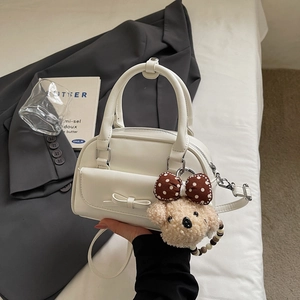 Detail of white Boston bag featuring a bow pocket, plush bear charm, and top handles