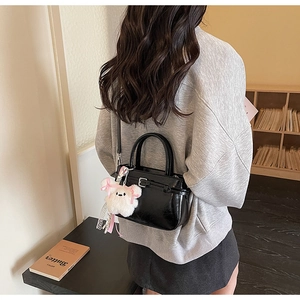 Detail of black glossy leather crossbody bag with white plush bear charm on model