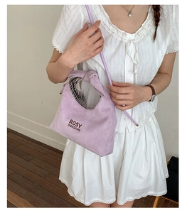 Close-up of lilac matte crossbody bag with knot handle and striped lining on white dress