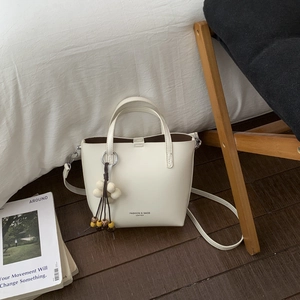 Close-up of cream white bucket bag with leather texture and floral charm detail