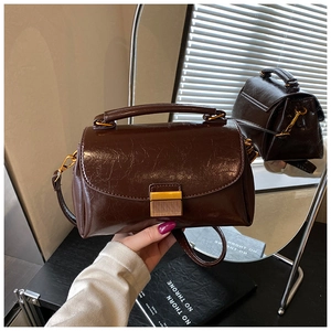 Détail de la texture cuir marron foncé et de la boucle en métal doré sur le sac à main