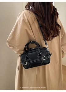 Sac rétro chic en cuir noir avec surpiqûres blanches contrastées sur manteau beige
