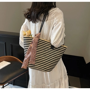Detail of handwoven black and white striped straw tote bag with a patterned silk scarf