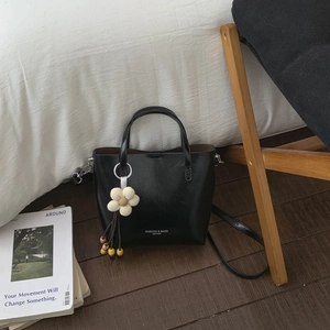 Detail of black faux leather bucket bag with white flower charm and tassel in a lifestyle setting