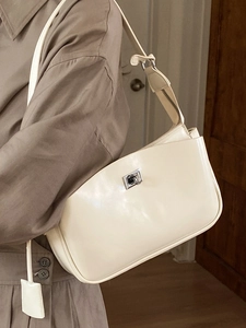 Elegant cream baguette shoulder bag with silver clasp styled on a classic trench coat