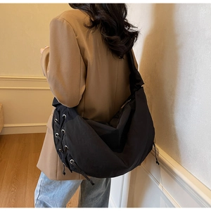 Détail du grand sac hobo noir avec lacets et oeillets métalliques porté par un mannequin