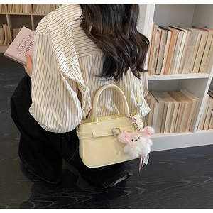 Detail of cream crossbody bag with plush bear charm and decorative buckle strap