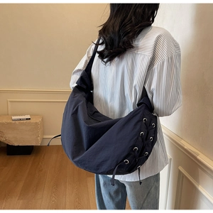 Détail d'un sac dumpling bleu marine en nylon avec laçage latéral porté à l'épaule
