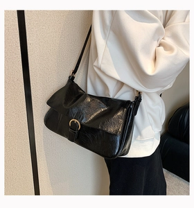 Polished black crossbody bag with gold buckle on model, minimalist shoulder bag style