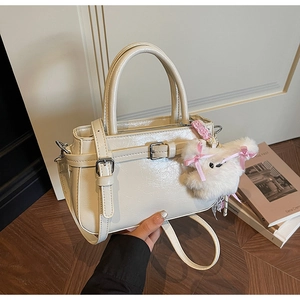 Detail view of cream white glossy leather crossbody bag with cute plush bear charm decoration