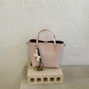 Close-up of pink bucket bag featuring a white flower pendant and leather text detail
