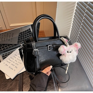 Detail view of a black embossed crossbody bag with silver buckle and white plush bunny charm