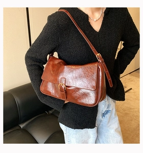 Detail shot of brown glossy oil-waxed leather shoulder bag with metallic buckle closure