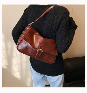Detailed back view of a vintage brown leather crossbody bag worn by a model in soft light