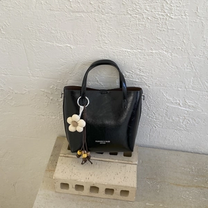 Detailed close-up of a black leather bucket bag with a cream floral charm on a stone base