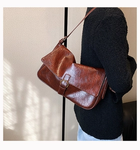Brown vintage leather shoulder bag with buckle detail worn by model against a white wall
