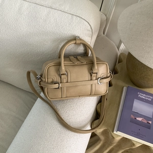 Vue détaillée d'un sac Boston beige sur un canapé blanc avec des boucles en métal argenté