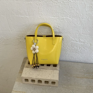 Close-up of lemon yellow leather bucket bag with fashion logo and white floral charm detail