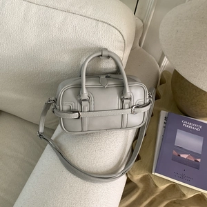 Détail d'un sac bowling en cuir gris clair avec boucle argentée sur un canapé blanc