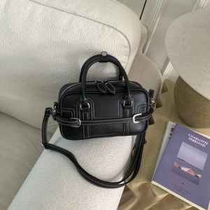 Vue détaillée d'un sac bowling en cuir noir avec surpiqûres blanches sur un canapé