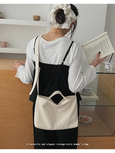 Close-up of a creamy white faux leather tote bag being carried in a cozy indoor setting