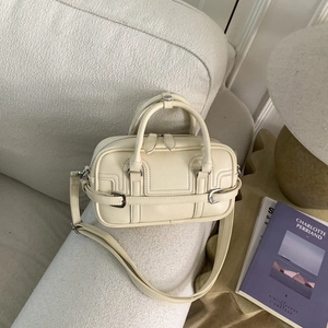Sac bowling chic en cuir crème avec boucles argentées sur canapé en laine blanche