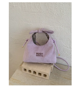 Detail view of purple matte crossbody bag with bow handle and brand logo on stone