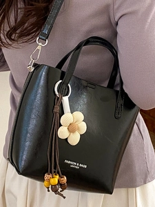 Chic black leather bucket bag with top handles, floral charm and crossbody strap