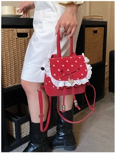 Détail du sac à dos rouge à pois avec dentelle et pendentif cœur tenu par un mannequin