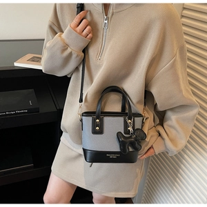 Détail du sac bandoulière bicolore avec pendentif chien noir porté par un mannequin