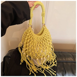 Dettaglio della borsa gialla intrecciata con lunghe nappe e perle in legno sul fondo