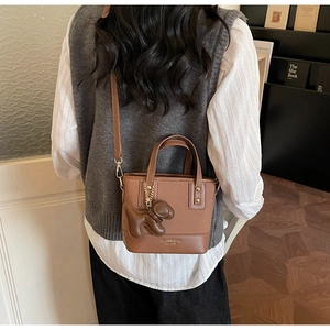 Petit sac carré marron en cuir PU avec breloque chien porté par un mannequin en intérieur