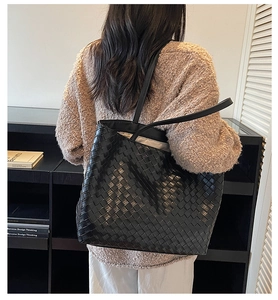 Detailed view of hand-woven black leather tote bag worn by a model in a minimalist setting