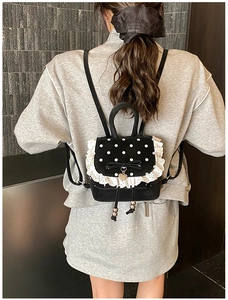 Détail d'un mini sac à dos noir à pois blancs avec bordures en dentelle et un nœud