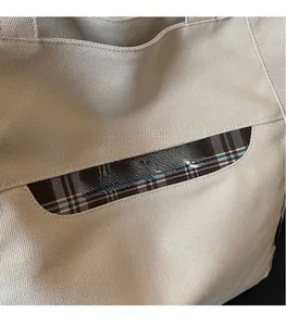 Dettaglio ravvicinato della borsa tote in tela con tasca scozzese marrone e ricamo