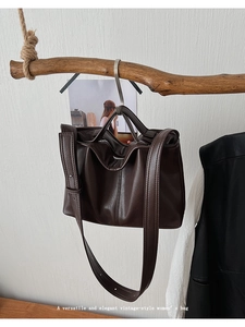 Detail view of dark brown vintage shoulder bag hanging on a branch with smooth leather texture