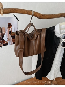 Close-up of a vintage brown leather tote bag hanging on a branch with artistic props