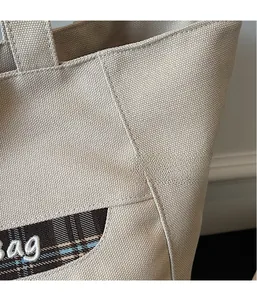 Dettaglio ravvicinato della borsa tote in tela beige con cuciture a contrasto e ricami