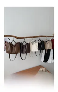 Five minimalist leather tote bags in various colors hanging on a wooden branch
