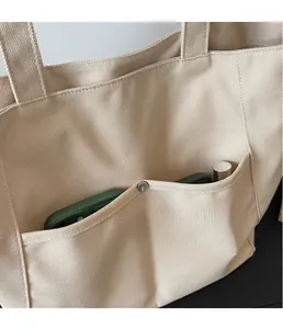 Dettaglio della borsa tote in tela beige con tasca anteriore e bottone a scatto in metallo