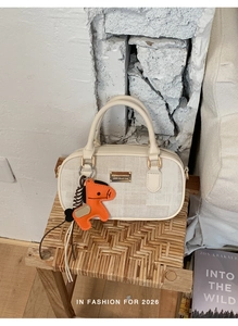 Detail of off-white Boston bag with gold metal plate and orange horse charm on a wooden stool