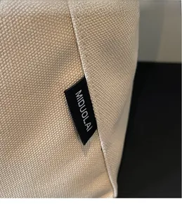 Dettaglio della borsa tote in tela beige con trama intrecciata ed etichetta logo