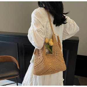Detailed view of beige woven tote bag with tassel fringe carried by model in white dress