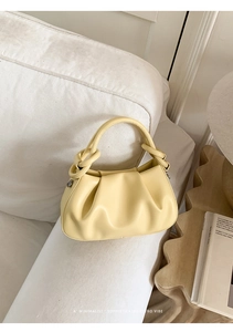 Dettaglio di una borsa a nuvola increspata giallo chiaro su un divano bianco in ecopelle