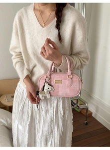 Detail of a light pink mini Boston bag with golden nameplate and horse charm accessory