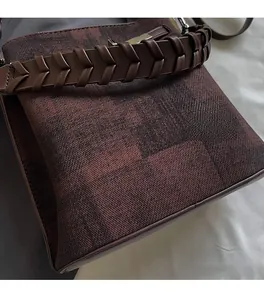 Detail view of deep reddish-brown fabric bucket bag with braided leather strap and metal buckle