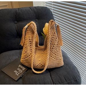 Detail of woven khaki shoulder bag with tassel fringe on a velvet sofa setup