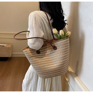 Close-up of woven straw tote bag with brown leather straps and fringed edge detail